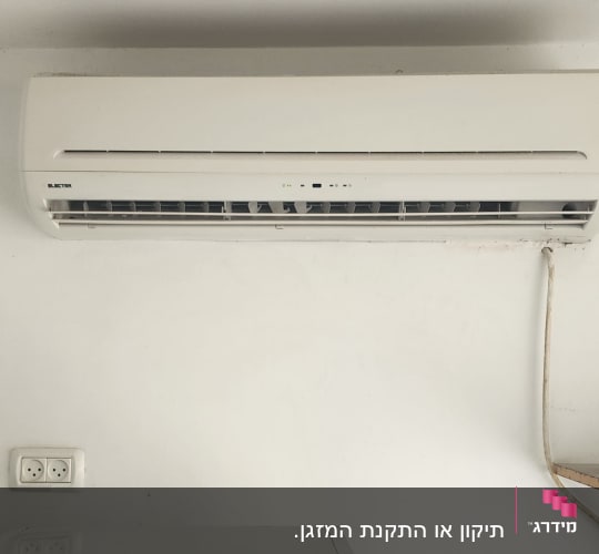 מזגן מותקן על קיר לבן מעל מקרר קטן